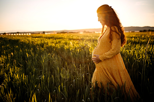 Pregnant woman holding stomach in middle of meadow