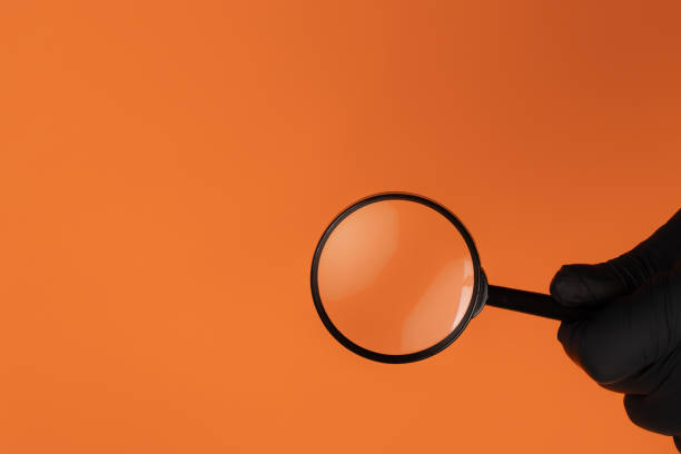 istock Magnifier on an orange background. A hand with a magnifying glass on an isolated background. Horizontal. Copy space 1321725362
