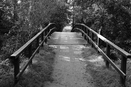 a black and white of a small romantic wooden bridge over a small river