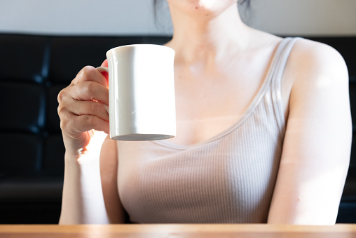 A woman relaxing with a cup of coffee in the living room of her house in the morning.\nThe hand of the person holding the coffee. Back bokeh. Selective focus.