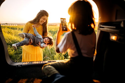 Mother and kids sitting in car trunk in the middle of meadow and playing