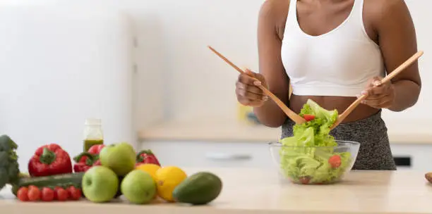 Healthy Diet. African Lady Cooking Salad Slimming At Home, Posing Wearing Fitwear Standing In Modern Kitchen Indoors, Smiling To Camera. Weight Loss Nutrition And Dieting Concept