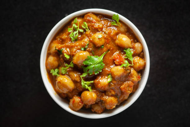 istock Chickpeas masala (Spicy chola or chhole curry) garnished with fresh green coriander and ingredients. Served in white ceramic bowl. Classic Indian typical Punjabi street food. 1321729486