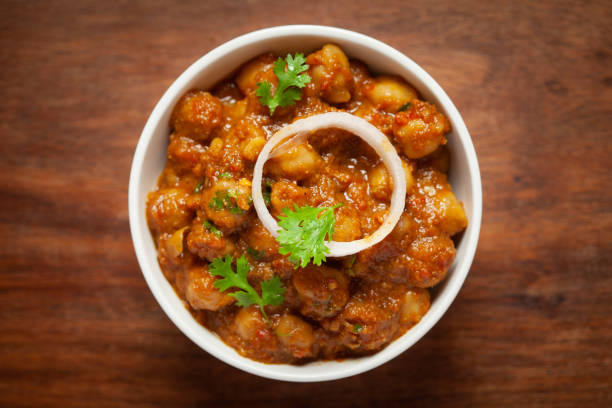 istock Chickpeas masala (Spicy chola or chhole curry) garnished with fresh green coriander and ingredients. Served in white ceramic bowl. Classic Indian typical Punjabi street food. 1321729494