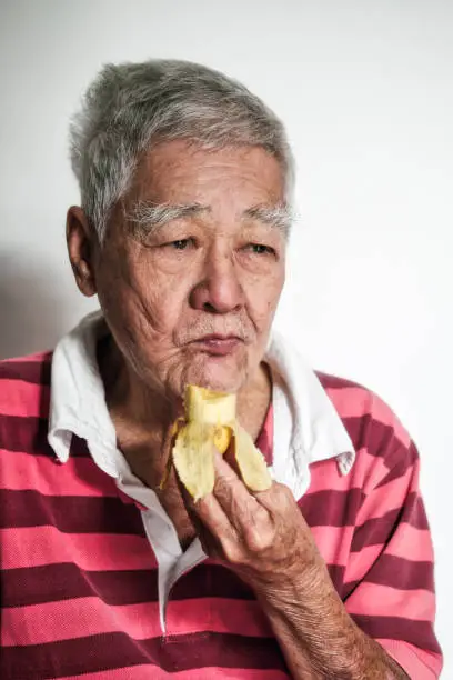 Portrait of an elderly Asian man eating banana