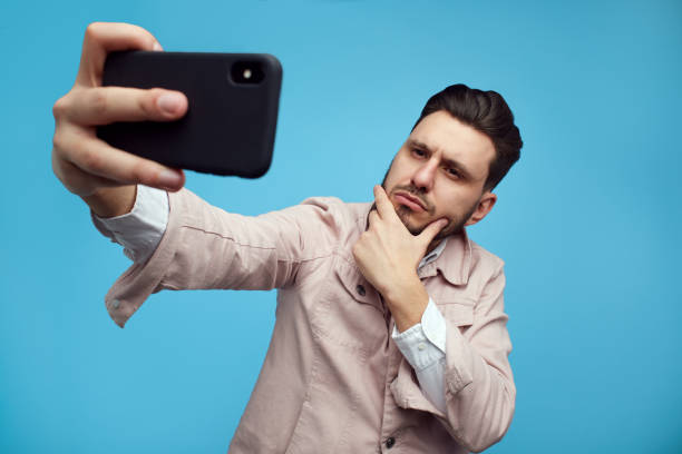 istock Serious confident bearded man taking a selfie with smartphone over blue 1321734421