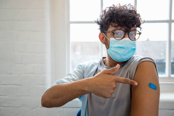 A Step Closer to Beating Coronavirus A man sitting in the doctor's office pointing to his arm that has a blue plaster on it. He has just had the COVID-19 vaccine. rolled up sleeves stock pictures, royalty-free photos & images