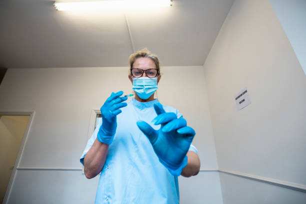 A personal perspective of a nurse wearing a protective face mask, holding a syringe, about to inject a patient with the COVID-19 vaccine.
