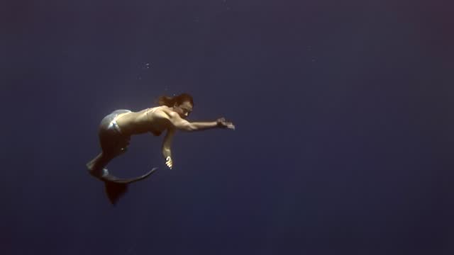 Young girl model underwater mermaid costume on blue background poses in Red Sea.