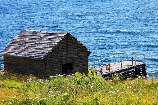 A log fishing shed, stage, and wharf on the water's edge, Random Passage Site, New Bonaventure, NL.