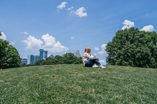 Woman Sitting On Grass In the Park, Midtown In Background