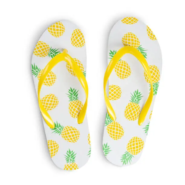 Colorful vivid pair of flip-flops type of sandal consisting of thin rubber sole with bright yellow pineapple print usually worn at hot summer season weather at the beach cut out on white background