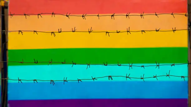 Photo of multicolored gay community flag behind barbed wire