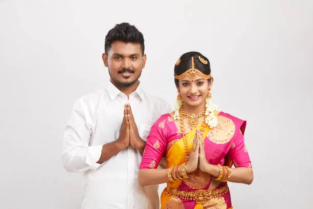 Beautiful happy south Indian couple in traditional dress giving greetings on white.