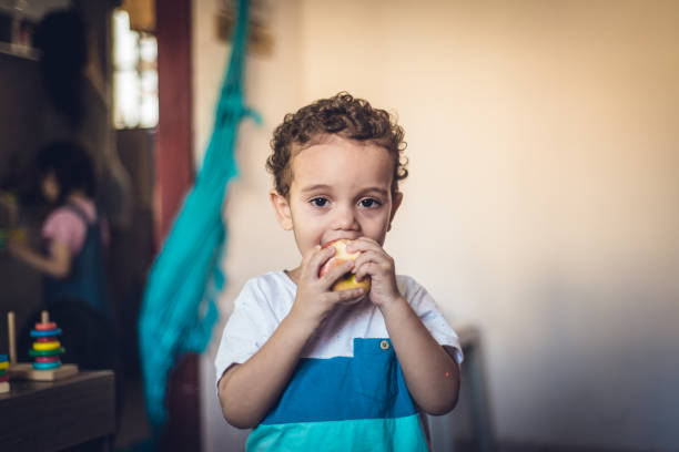 Portrait of small child boy eating apple looking at camera.