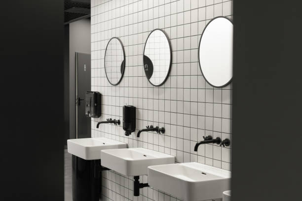 istock Modern public restroom minimal interior with metro style white tiles, round mirrors, black ceiling and half opened door with modern toilet signs 1321757612