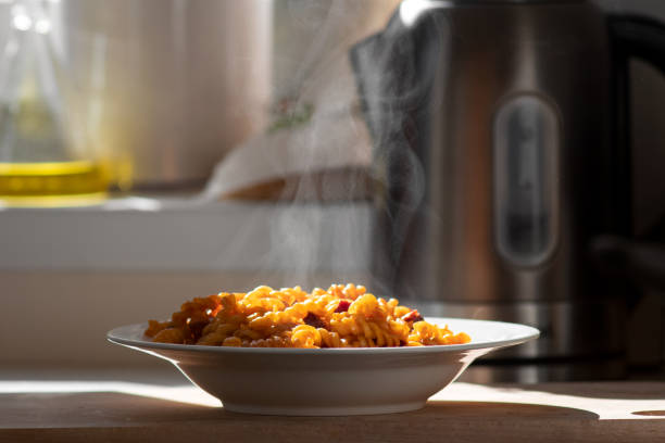 Healthy homemade Mediterranean dish Fusilli pasta with tomato sauce and salami in white plate with steam and smoke on the kitchen table. Selective focus. serving dish stock pictures, royalty-free photos & images