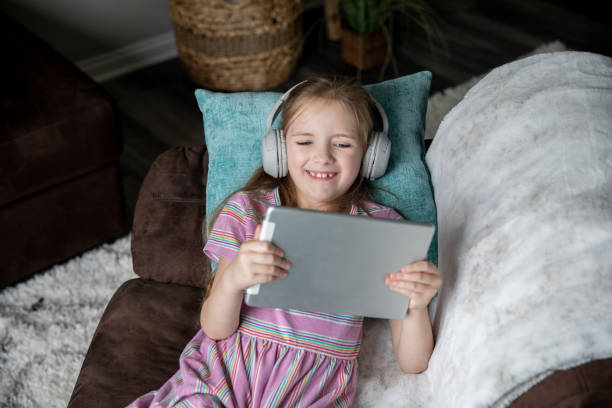 istock Elementary aged girl 
 wearing headphones watching her tablet 1321763591