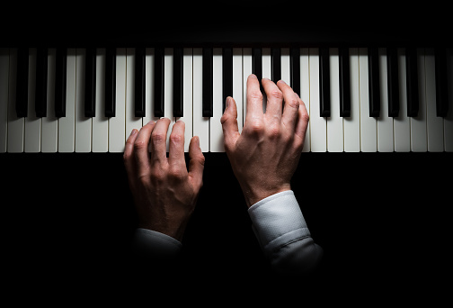 Pianist's two hands playing on piano, playing chords, in mood light, isolated hands