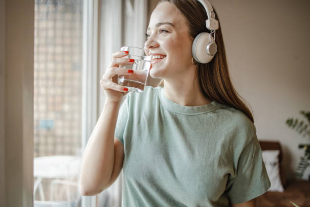 istock Young woman drinks water from a glass by the window 1321767144