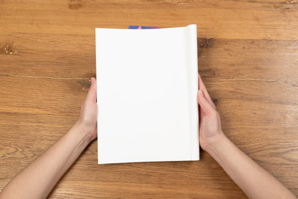 istock Woman's hands open empty catalog, magazines, book mockup on wooden table 1321768535