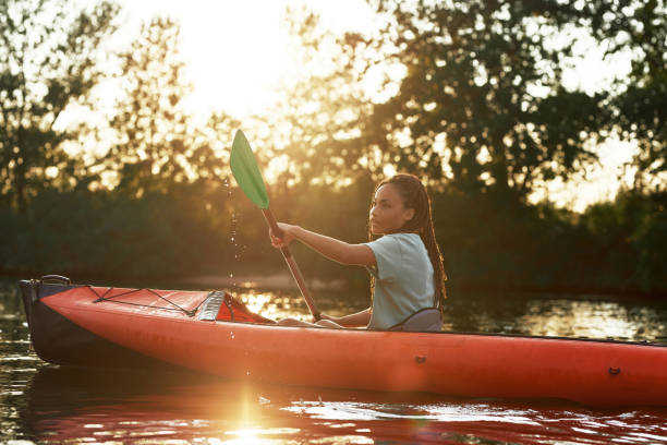 Attractive young woman holding a paddle while kayaking in a lake surrounded by nature on a late summer afternoon