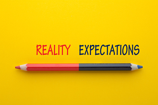 The words Expectation vs Reality with pencil on yellow background.