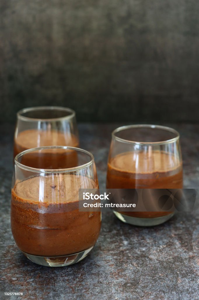 Image of three glasses containing home-made chocolate mousse dessert, dark grey background, focus on foreground Stock photo showing a studio shot of three glasses containing a chocolate mousse dessert. Chocolate Mousse Stock Photo