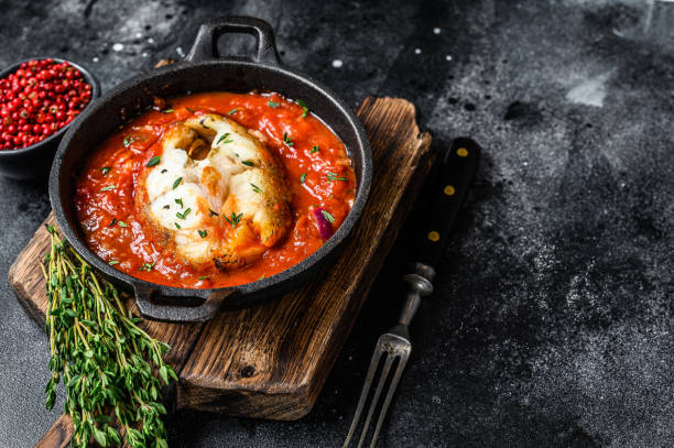 istock Baked hake white fish with tomato in a pan. Black background. Top view. Copy space 1321780299