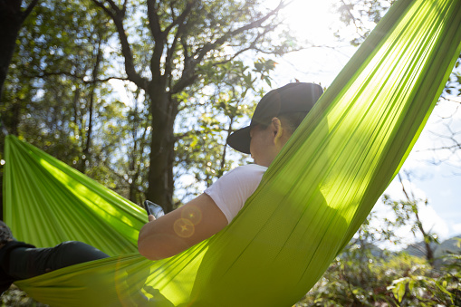 Hammocking and using mobile phone  in summer tropical forest
