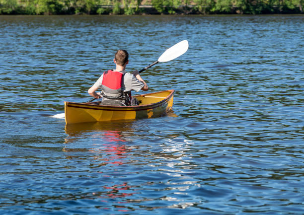 un homme caucasien pagayant un canot de meute avec une pagaie de kayak sur le lac - canoe kayak, jaune photos et images de collection