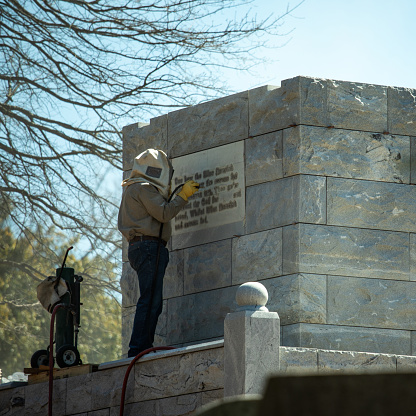 Atlanta, United States - March 2020: Man with safety equipment engraving a plaque at the cemetery