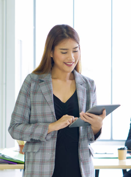 istock A female employee in a plaid pattern suit standing with tablet computer in her hand. Morning work atmosphere in a modern office. 1321827998