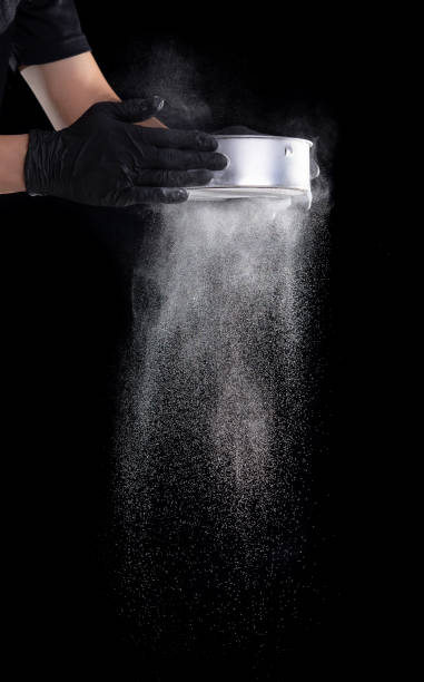 istock Flour sifting through a sieve for a baking on black background 1321838197