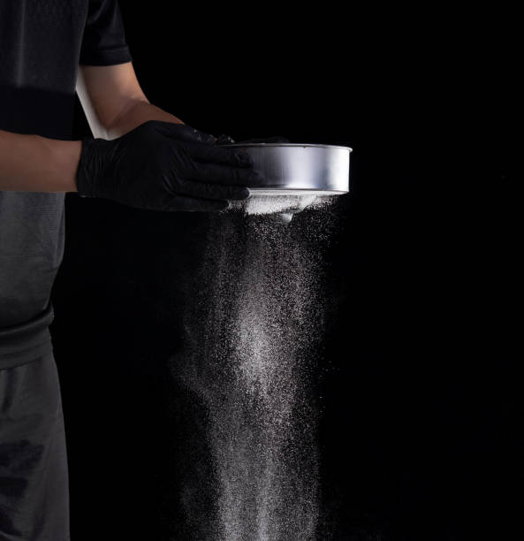 istock Flour sifting through a sieve for a baking on black background 1321838210