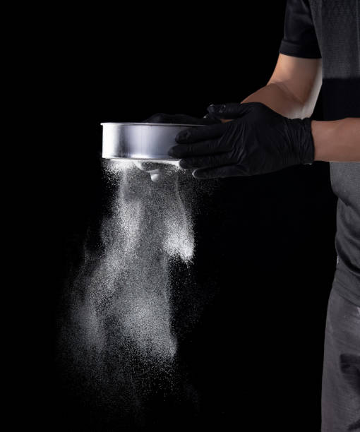 istock Flour sifting through a sieve for a baking on black background 1321838243