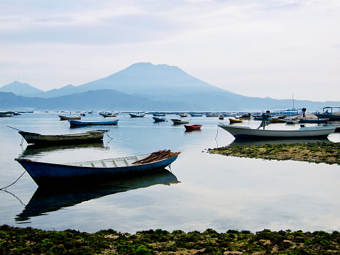 Horizontal landscape photo of moored wooden boats used for fishing and seaweed farming by Balinese people living on the island of Nusa Lembongan across from the coast of Bali. On the horizon the highest active volcano in Bali, Gunung  Agung.