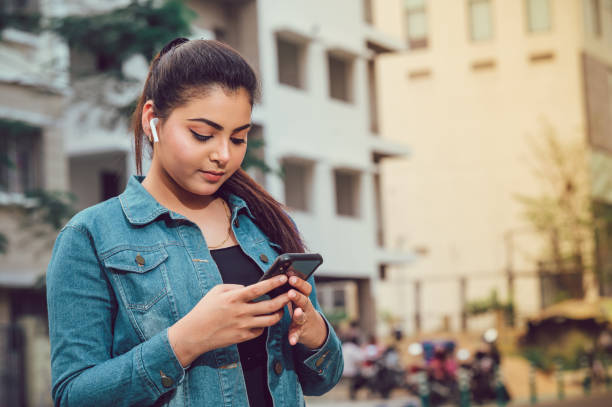 beautiful cute smiling woman is using mobile phone outside on road. - indian ethnicity audio imagens e fotografias de stock