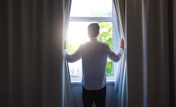 istock Young man open curtain in the morning 1321850927