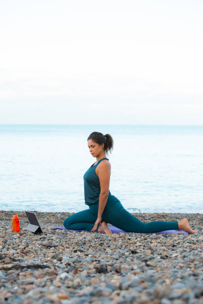 istock a mixed-race woman does yoga on the beach while watching exercises on a tablet at dawn 1321860493