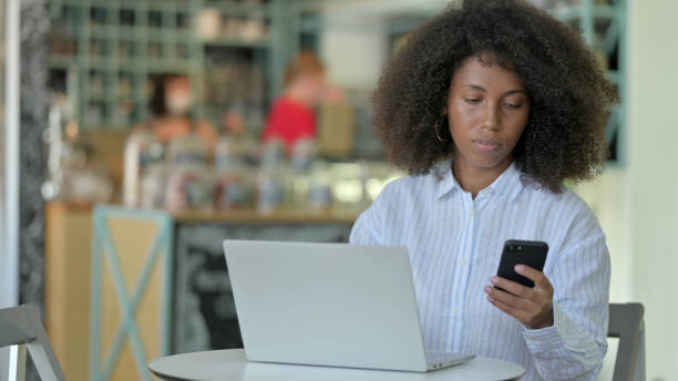istock Young African Woman using Smartphone and Laptop in Cafe 1321863775