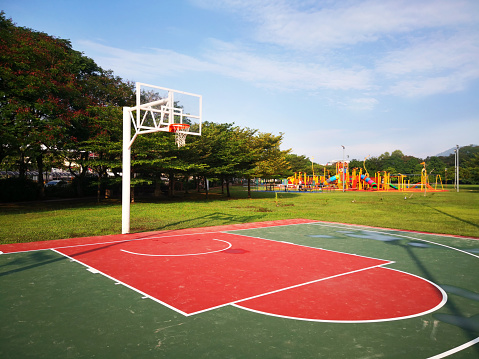 Outdoor public basket ball court near residential area with playground in the background