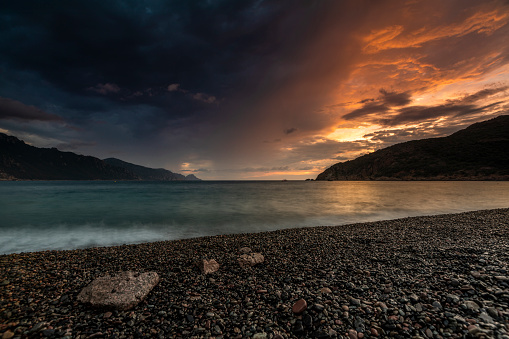 Beautiful sunset clouds over a gravel beach at the western coastline of the corse du sud province in Corsica, France.