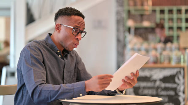 istock Surprised Young African Man Reading Documents in Cafe 1321866869