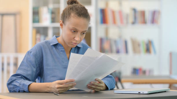 istock Young African Woman Reading Documents in Library 1321866993