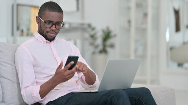 istock African Man using Smartphone and Laptop at Home 1321868318