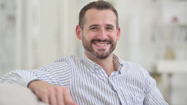 istock Young Man Sitting on Sofa and Smiling at Camera 1321868442