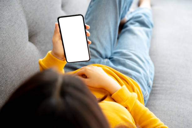 istock Mock up image white screen mobile smartphone. Woman using smart phone and relaxing on sofa. Clipping path included device screen 1321870176