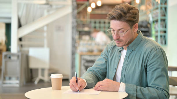 istock Serious Middle Aged Man Writing on Paper in Cafe 1321871419