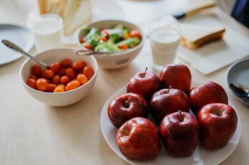 Healthy breakfast on top of dining table. Apples, cherry tomatoes, salad bowl.